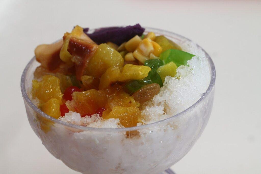 Glass of halo-halo with shaved ice topped with sweetened fruit, jellies and ube